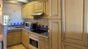 A kitchen with wooden cabinets, a microwave, a stove, and a window. - Mazet garden level sea view close to calanques and beach (Saint-Raphaël)