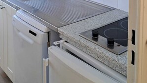 Una cocina con armarios blancos, un lavamanos de acero inoxidable, una estufa a gas y un horno empotrado.
