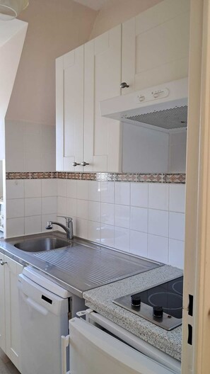 A kitchen with white cabinets, a stainless steel sink, a gas stove, and a built-in oven. - Charming apartment near Deauville (Blonville-sur-Mer)