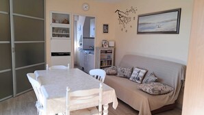 Una sala de estar acogedora con una mesa de comedor, sillas, un sofá con cojines estampados, una estantería y un cuadro en la pared.