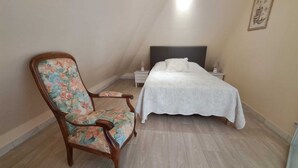 Un dormitorio con cama, una mesita de noche, una silla tapizada con motivos florales y una obra de arte colgada en la pared.