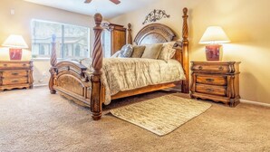 A bedroom with a four-poster bed, two nightstands, a ceiling fan, and a window with blinds.