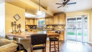 A kitchen with wooden cabinets, a central island, bar stools, and a ceiling fan.