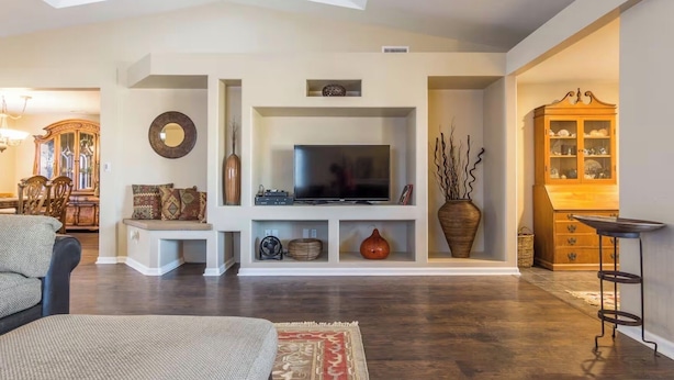 A living room with a TV, shelves, a cabinet, and a dining area with chairs and a table.