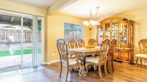 A dining room with a large table, chairs, a chandelier, and a wooden cabinet.