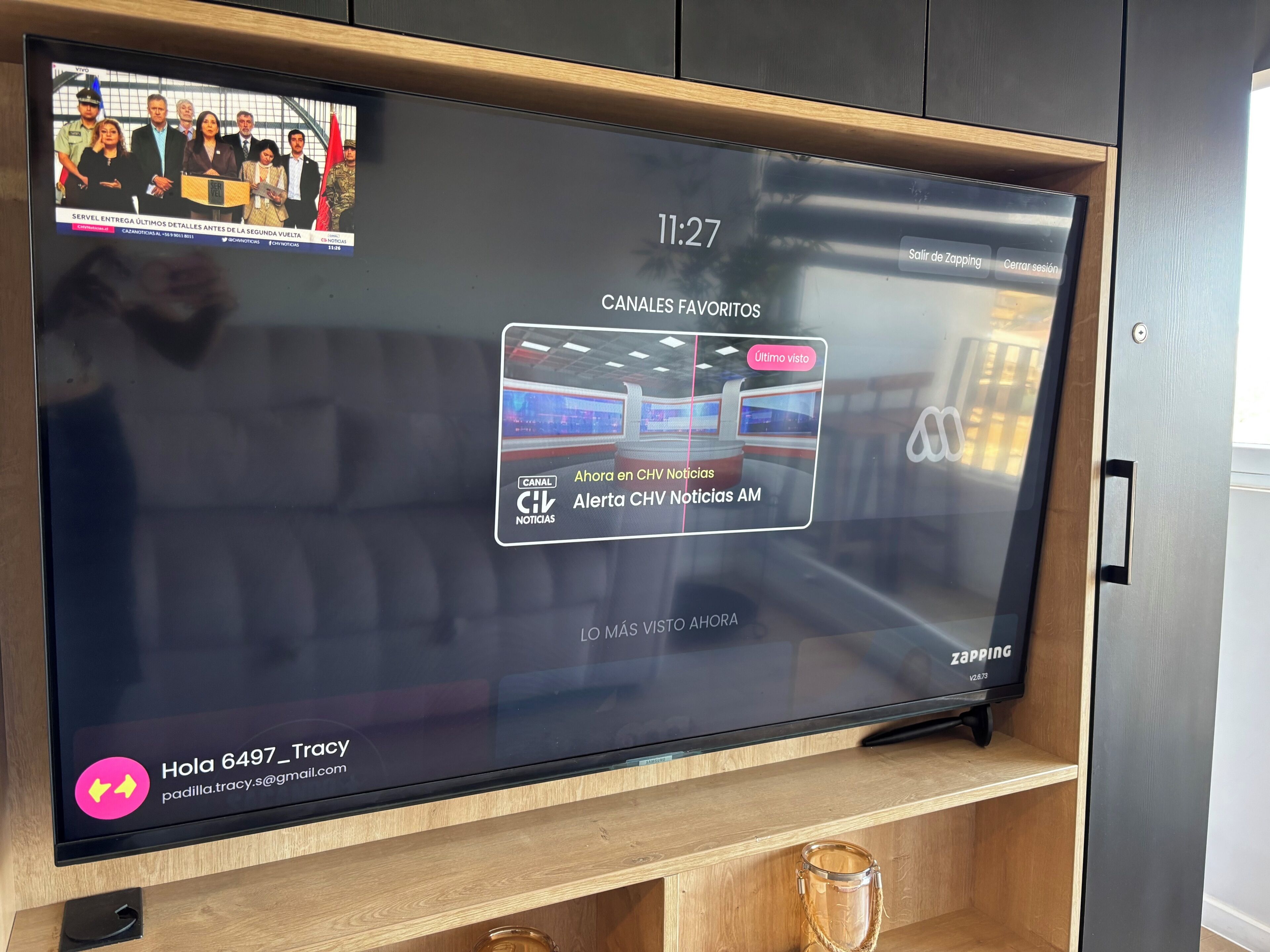 Un televisor mostrando una interfaz de canal de noticias con un grupo de personas, una marca de tiempo y una dirección de correo electrónico de contacto.