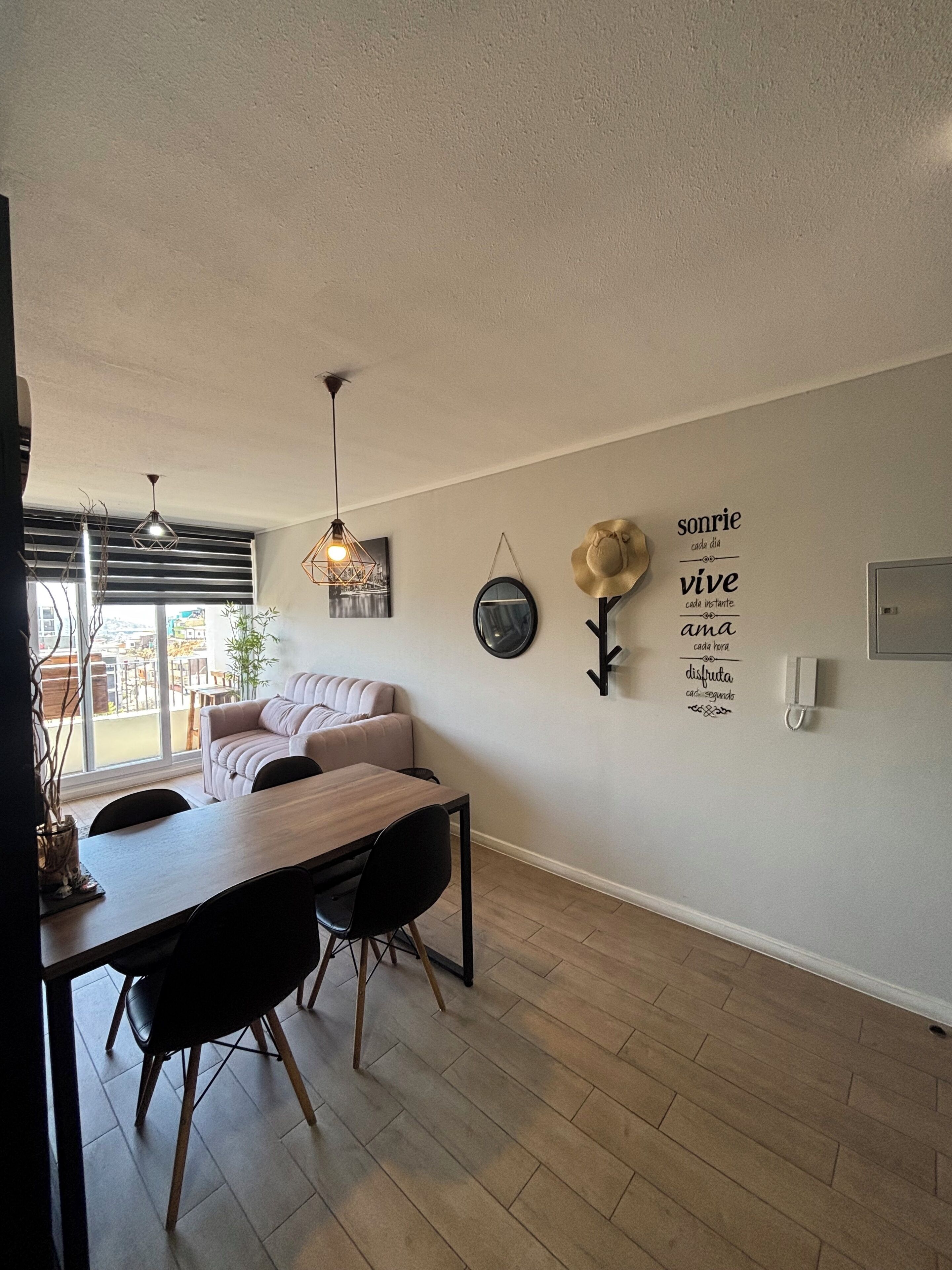 Un comedor moderno con una mesa y sillas de madera, un sofá y una lámpara fijada a la pared.