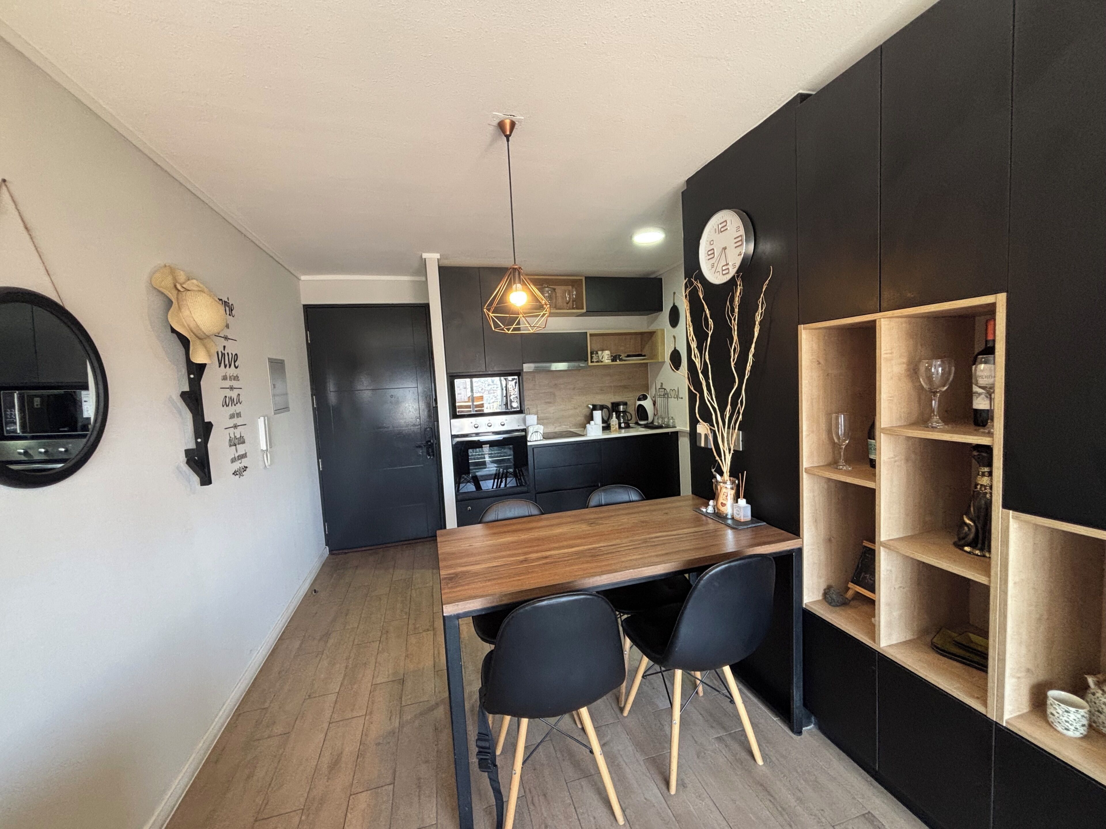 A modern kitchen with a dining area, wooden furniture, and a wall-mounted clock.