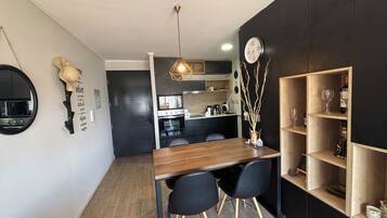 A modern kitchen with a dining area, wooden furniture, and a wall-mounted clock.
