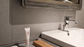 Un baño con un espejo grande, un lavamanos blanco y una encimera con una loción y cajas.