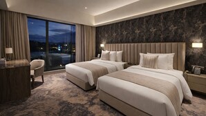 A hotel room with two beds, a desk, a chair, a large window with a view, and a dark patterned wall. - colombo international airport hotel (Katunayake)