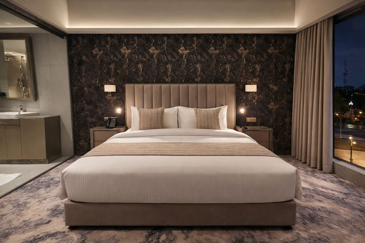 Ein großes Bett mit gepolstertem Kopfteil, Nachttischlampen, einer Wand mit Marmor-Muster und Blick auf die Stadt durch ein Fenster.
