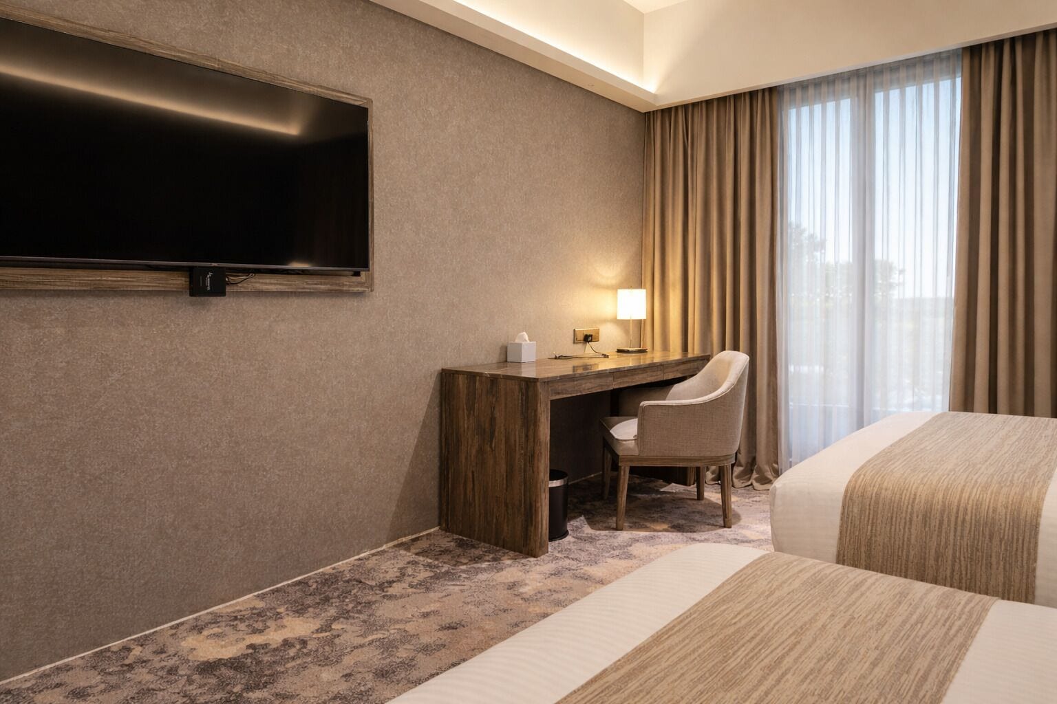 A hotel room with a bed, a desk, a chair, a television, and a window with curtains.