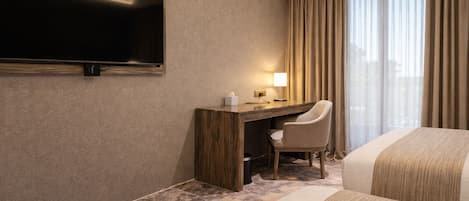 A hotel room with a bed, a desk, a chair, a television, and a window with curtains.