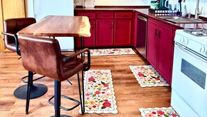 Una cucina con pavimento in legno, un tavolo da pranzo con sedie, mobili rossi, un frigorifero bianco e un piano cottura.