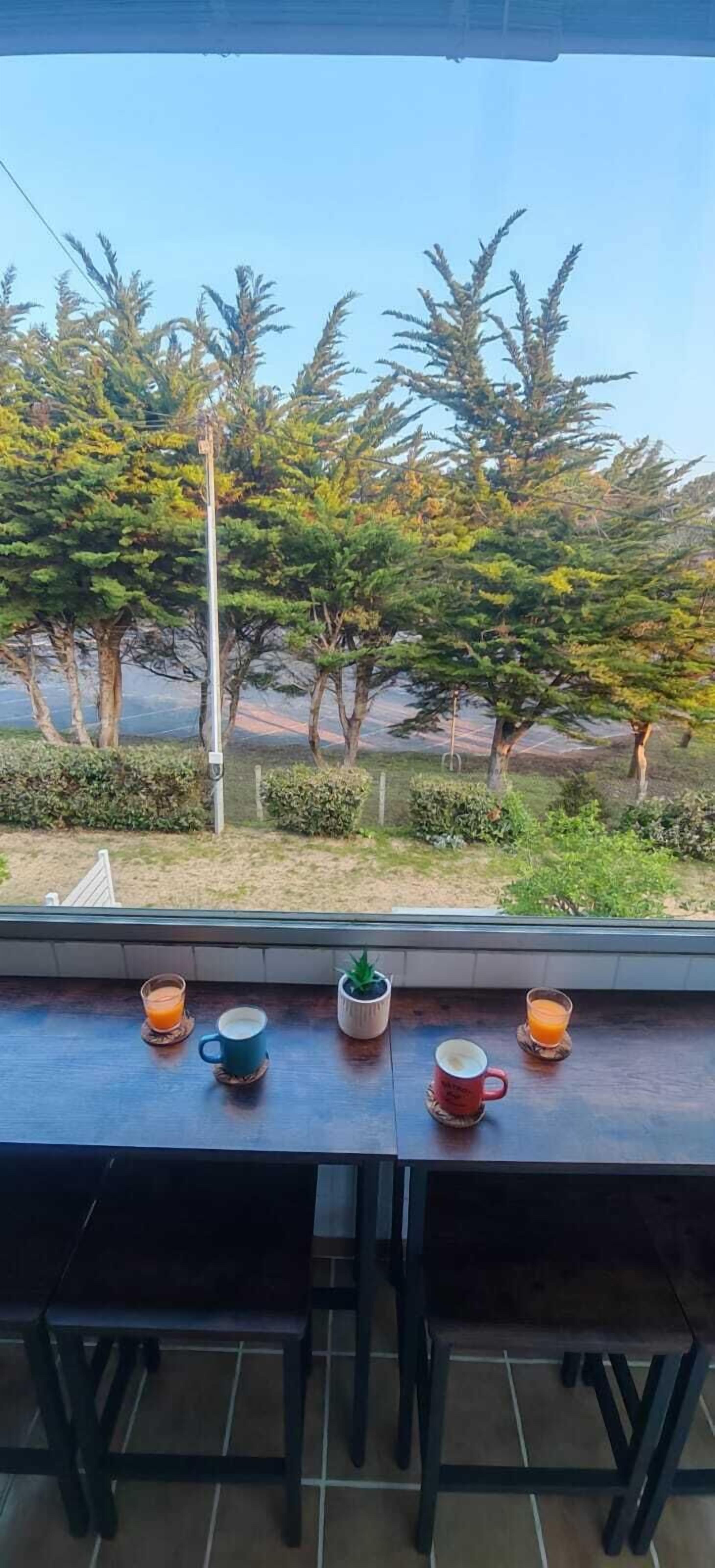 A balcony with a wooden table, two chairs, and a view of trees and a road.