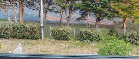A balcony with a wooden table, two chairs, and a view of trees and a road.