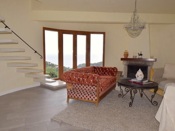 A living room with a sofa, a fireplace, a chandelier, and a staircase. - Villa Oleander (Begur, Es Valls Begur, Costa Brava) (Begur)