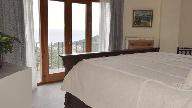 A bedroom with a large bed, a wooden dresser, a painting on the wall, and a balcony with a view. - Villa Oleander (Begur, Es Valls Begur, Costa Brava) (Begur)