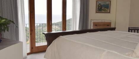 Une chambre avec un grand lit, une commode en bois, un tableau au mur et un balcon avec vue.
