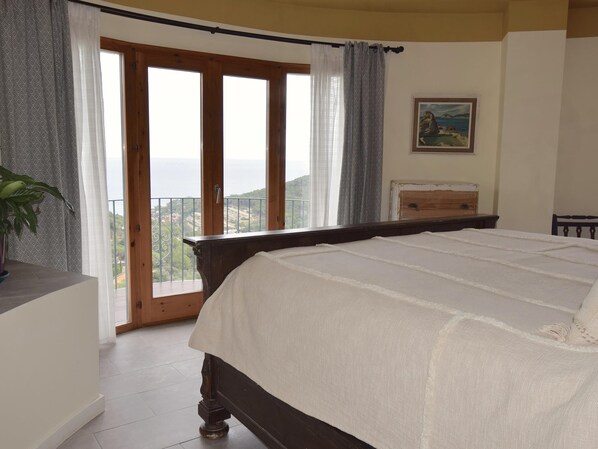 Ein Schlafzimmer mit einem großen Bett, einer Holzkommode, einem Bild an der Wand und einem Balkon mit Blick.