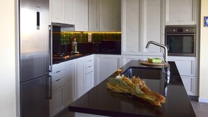Eine moderne Küche mit weißen Schränken, einem Edelstahlkühlschrank, einer schwarzen Arbeitsplatte und einem eingebauten Backofen.