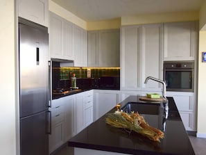 Een moderne keuken met witte kasten, een roestvrijstalen koelkast, een zwart aanrecht en een inbouwoven.