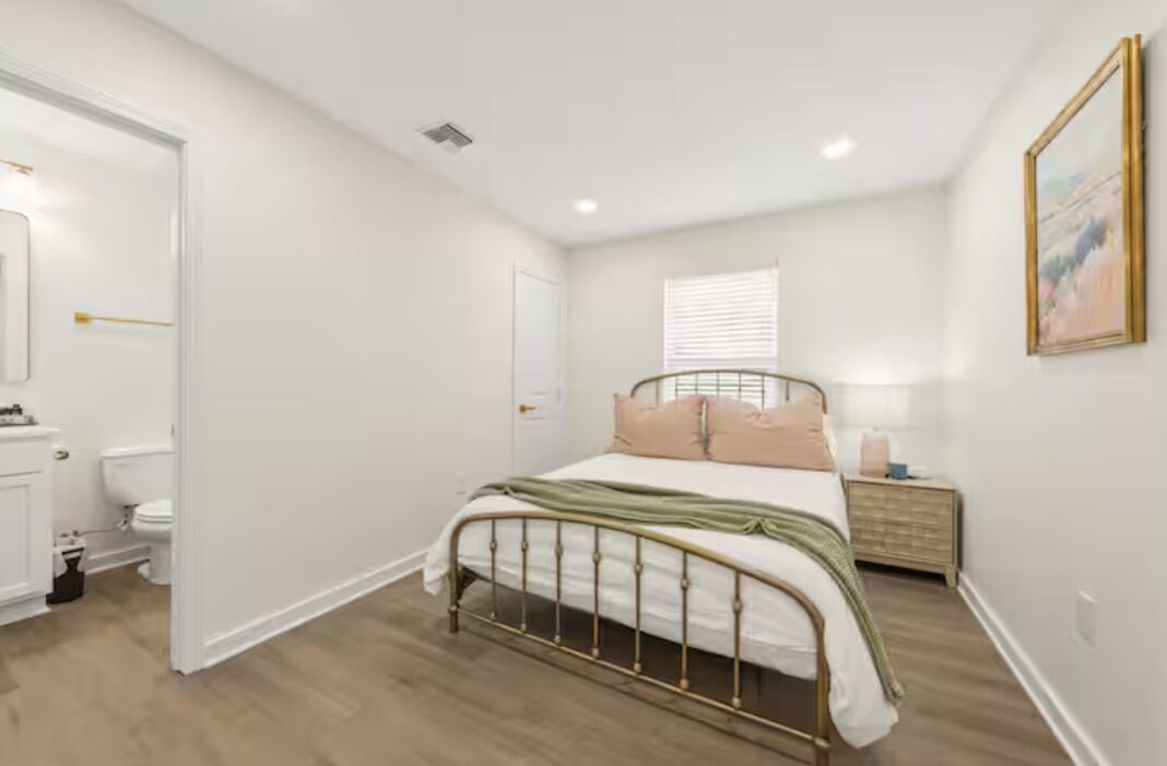 Un dormitorio con cama, mesita de noche, ventana y puerta que da a un baño.