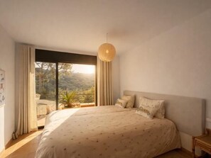 A bedroom with a large bed, a view of the outdoors, and a hanging light fixture. - Casa Santani (Begur, Sa Tuna) (Sa Tuna, Begur)