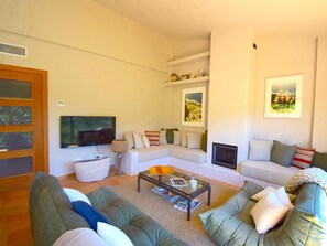 A living room with a sectional sofa, a flat-screen TV, a fireplace, and framed artwork on the walls. - Casa Santani (Begur, Sa Tuna) (Sa Tuna, Begur)