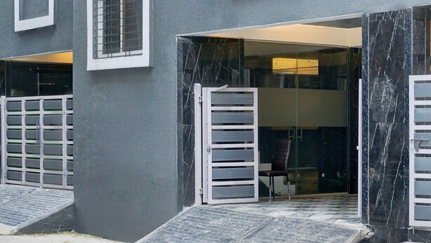 A building entrance with a ramp leading to a door, a small table, and a chair inside. - Deluxe Hinjewadi Corporate Stays (Paud)
