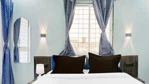 A hotel room with a bed, two bedside tables, a window with curtains, and wall-mounted lights. - Deluxe Hinjewadi Corporate Stays (Paud)