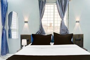 A hotel room with a bed, two bedside tables, a window with curtains, and wall-mounted lights. - Deluxe Hinjewadi Corporate Stays (Paud)