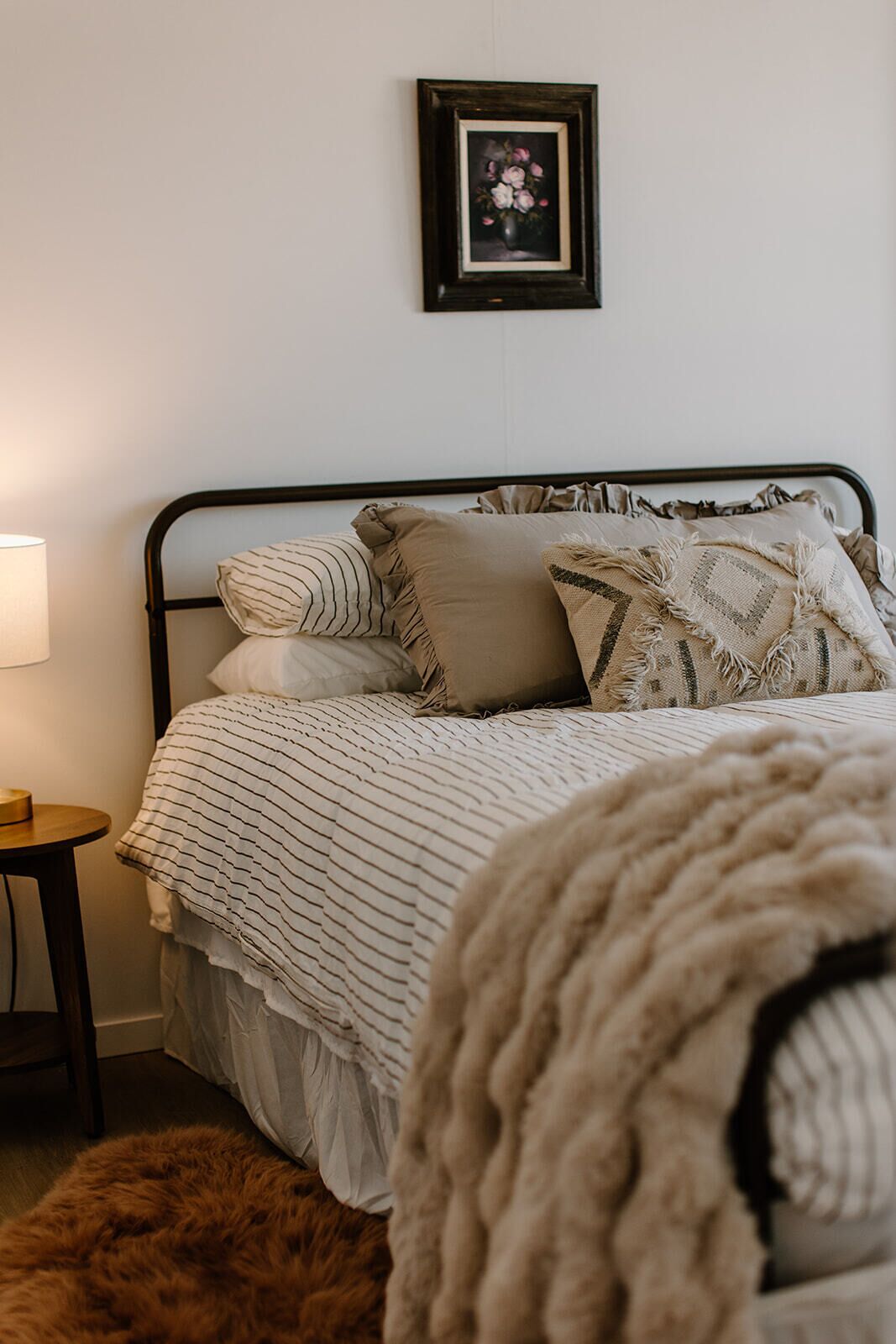 A bed with a striped blanket, a pillow with a geometric pattern, and a framed picture on the wall.