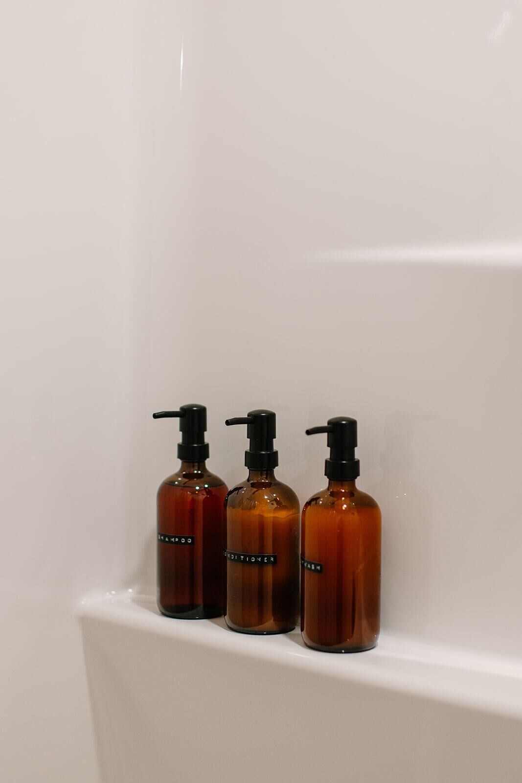 Trois bouteilles marron avec des pompes noires, posées sur une étagère blanche.