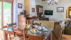 A dining area with a brick fireplace, wooden furniture, and a television in the background. - Los Rosales del Jaral El Gastor by Ruralidays (Cádiz)