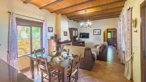 A dining area with a table and chairs, a sofa, and a television in a room with wooden beams and a tiled floor. - Los Rosales del Jaral El Gastor by Ruralidays (Cádiz)