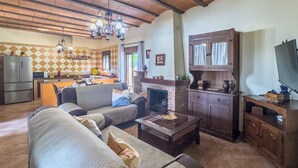 A living room with a sofa, a coffee table, and a fireplace. There is a kitchen area with a refrigerator and a stove. - Los Rosales del Jaral El Gastor by Ruralidays (Cádiz)