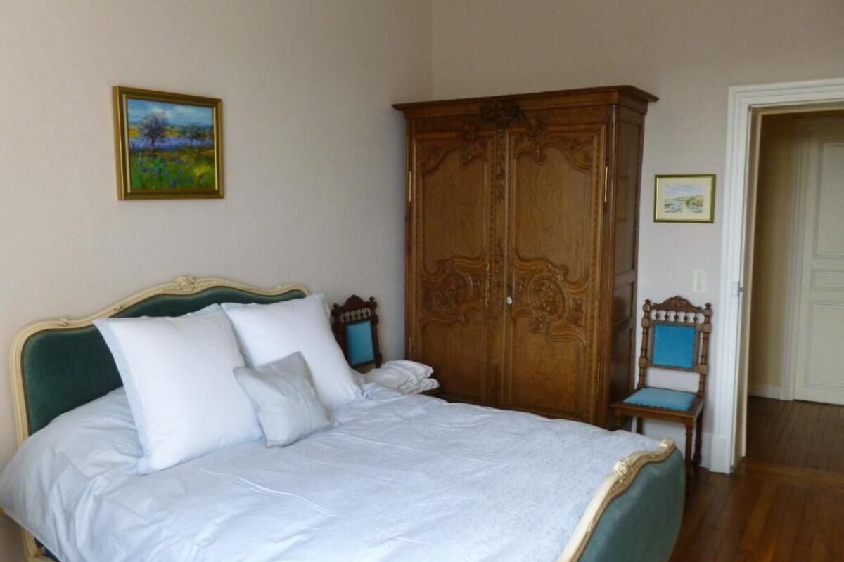 A bedroom with a bed, a wooden wardrobe, a chair, and two framed pictures on the wall.