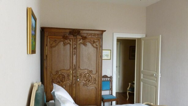 Un dormitori amb llit, armari de fusta, cadira i porta que dona a una altra habitació.