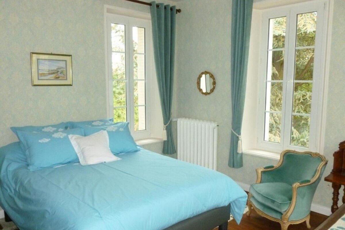 A bedroom with a bed, a chair, a window, a radiator, and a picture on the wall.