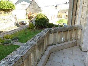 A balcony with a stone balustrade overlooking a garden and a street.