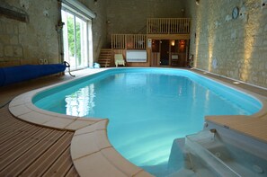 An indoor swimming pool with a wooden deck, a hot tub, and a view of the outside through a large window. - La Chambre au Château (Pernant)