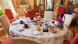 Taula de dinar arrapada per a les menjades, amb diversos plats i utensilis, envoltada de cadires vermelles a una habitació amb estovell estampat.