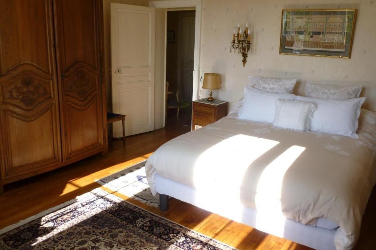 A bedroom with a bed, a wooden wardrobe, a nightstand with a lamp, and a patterned rug.