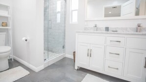 Une salle de bain moderne avec une douche à parois de verre, des meubles blancs et un comptoir en marbre.