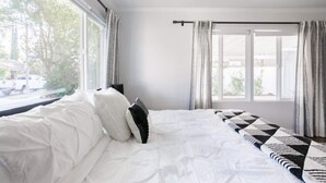 Une chambre avec un grand lit, du linge de lit blanc, une fenêtre avec des rideaux et une vue sur l’extérieur.