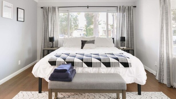 Une chambre à coucher avec un grand lit, une banquette, deux tables de chevet et une fenêtre avec des rideaux.
