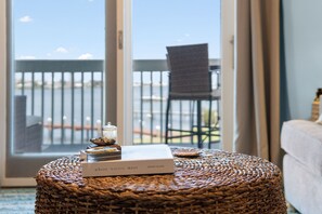 Une pièce comprenant un pouf en osier, un livre intitulé « Là où les eaux se rencontrent » de Jonah Allen, et une vue sur un balcon avec une chaise.
