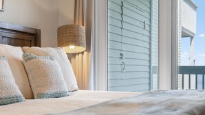 Una cama con almohadas, una lámpara tejida y vistas de un edificio a través de una ventana.